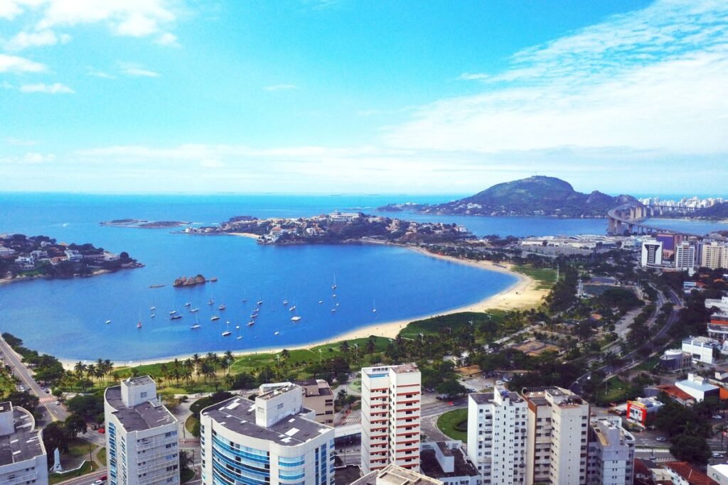 Vista panorâmica da Praia de Camburi em Vitória, Espírito Santo, com turistas aproveitando a orla e um belo pôr do sol ao fundo.